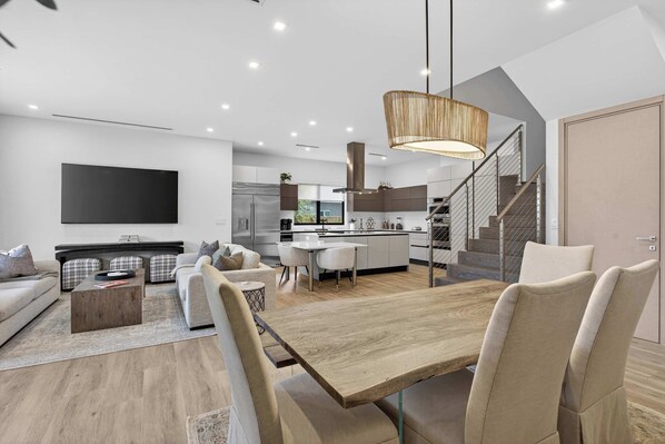 Una sala de estar moderna con un televisor de pantalla plana grande, una mesa de comedor de madera y una escalera que sube a un nivel superior.