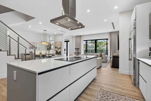 A modern kitchen with a central island, a staircase, and a living area with a sofa and a large window. - Tarpon River Enclave - New Build (Fort Lauderdale)