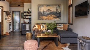 Ein gemütliches Wohnzimmer mit einer Couch, einem Couchtisch und einem aufgehängten Gemälde einer Berglandschaft.