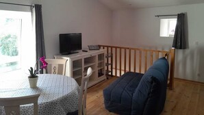 En stue med fjernsyn, et bord med en potteplante, en blå sofa og en trægelænder.