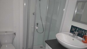Et badeværelse med toilet, bruseniche i glas og et håndvaskspejl.