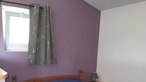 Et soveværelse med en træseng, et natbord, en lampe og et vindue med gardiner.