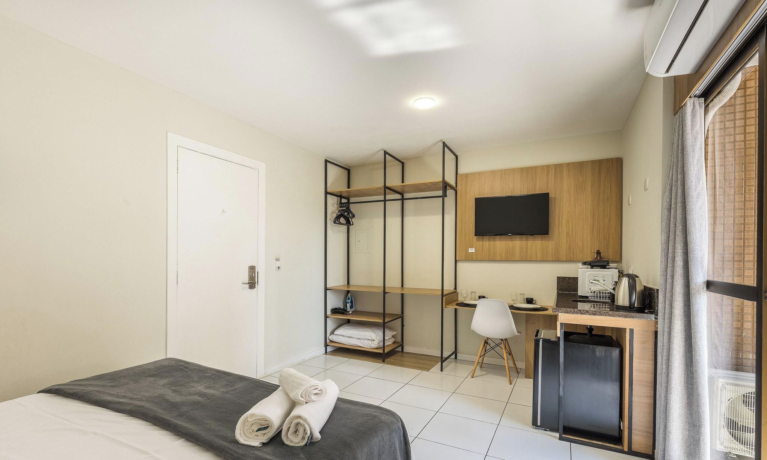A hotel room with a bed, a desk, a chair, a TV, and a shower area.