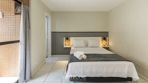 A hotel room with a bed, a nightstand, a wall-mounted lamp, and a window with curtains. - Studios at Upper Residence - Upps II (Curitiba)