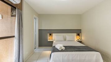 A hotel room with a bed, a nightstand, a wall-mounted lamp, and a window with curtains.
