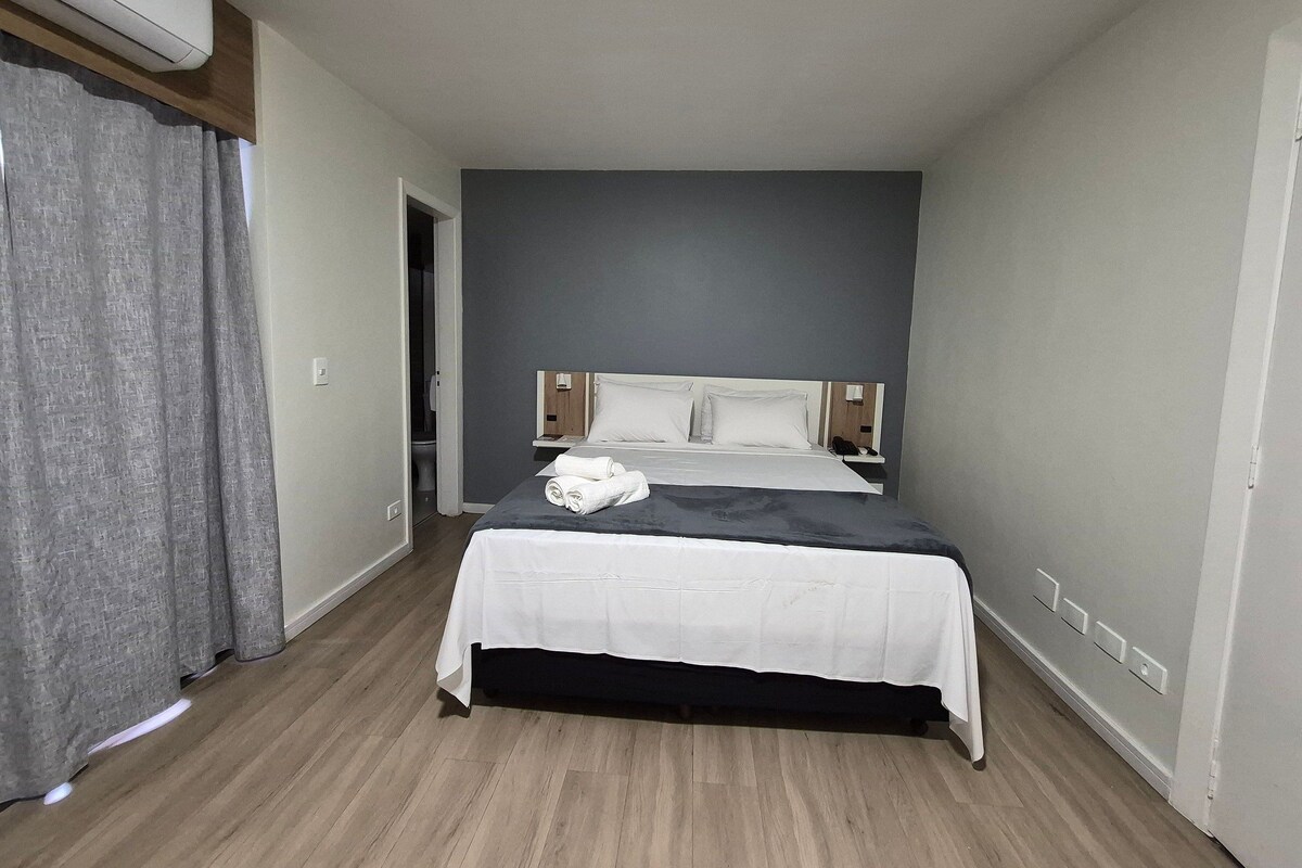 Une chambre d’hôtel avec un lit, une table de chevet, un téléphone et une fenêtre avec des rideaux.