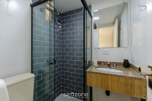 A modern bathroom with a glass shower enclosure, a white toilet, a sink with a wooden vanity, and a mirror.