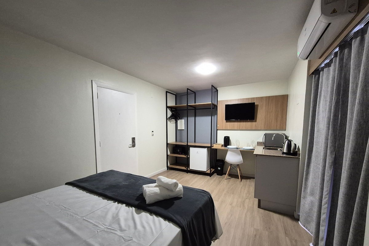 Een hotelkamer met een bed, een bureau, een stoel, een kleine koelkast, een televisie en een raam met gordijnen.