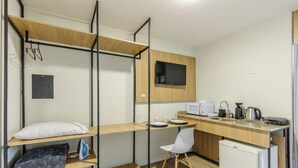 A compact room with a bunk bed, a desk, a chair, a television, a microwave, and a small refrigerator. - Studios at Upper Residence - Upps II (Curitiba)
