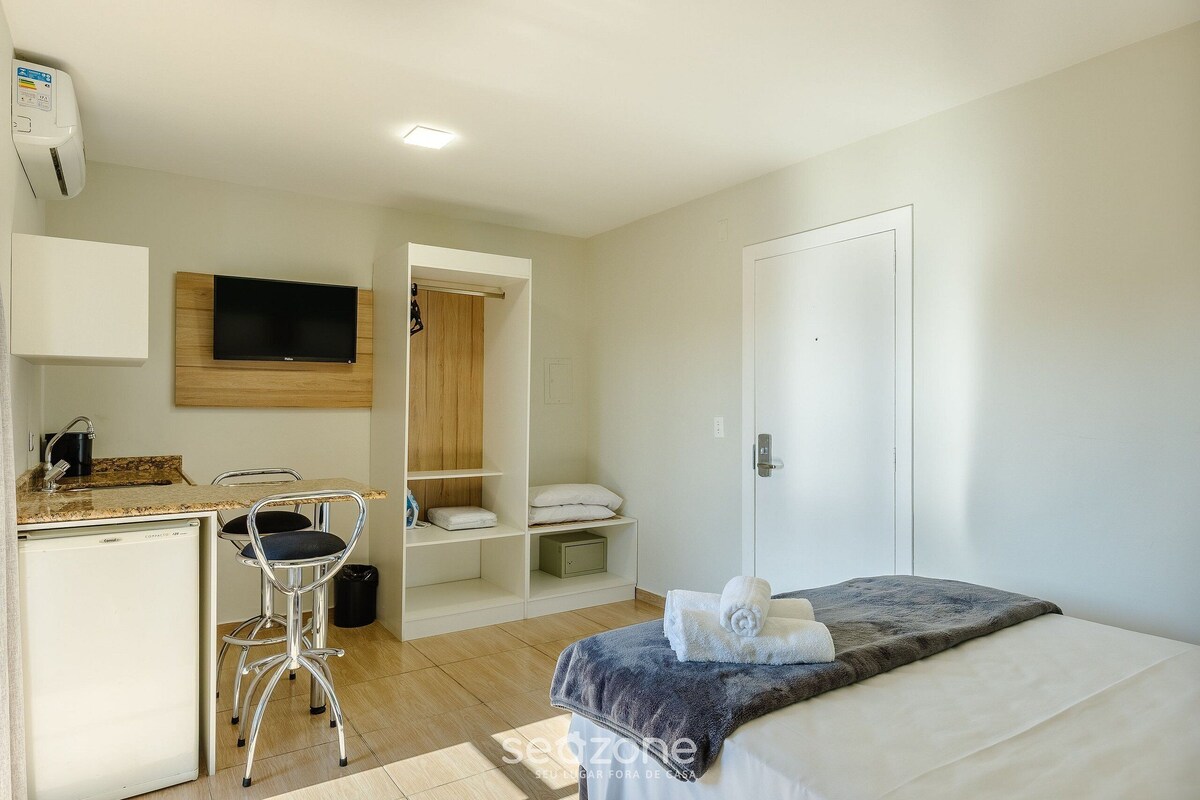 A compact hotel room with a bed, a small kitchenette, a TV mounted on the wall, and a closet.