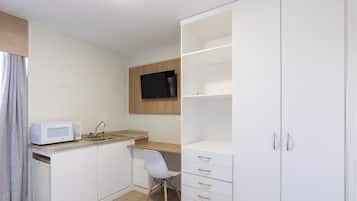 Habitación compacta con kitchenette, televisor de pantalla plana en la pared y un armario blanco con cajones.