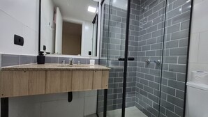 Un baño moderno con tocador de madera, cabina de ducha de vidrio y paredes con azulejos grises.