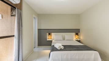 Una habitación de hotel con cama, mesita de noche, lámpara de pared y ventana con cortinas.