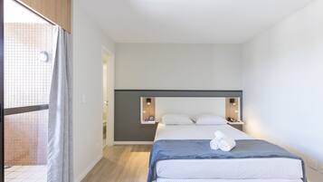 Quarto de hotel moderno com uma cama grande, uma pequena mesa de cabeceira e uma estante embutida.