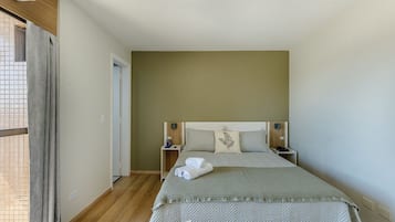 Um quarto com uma cama, duas mesas de cabeceira, um criado-mudo, uma janela com cortinas e uma porta.