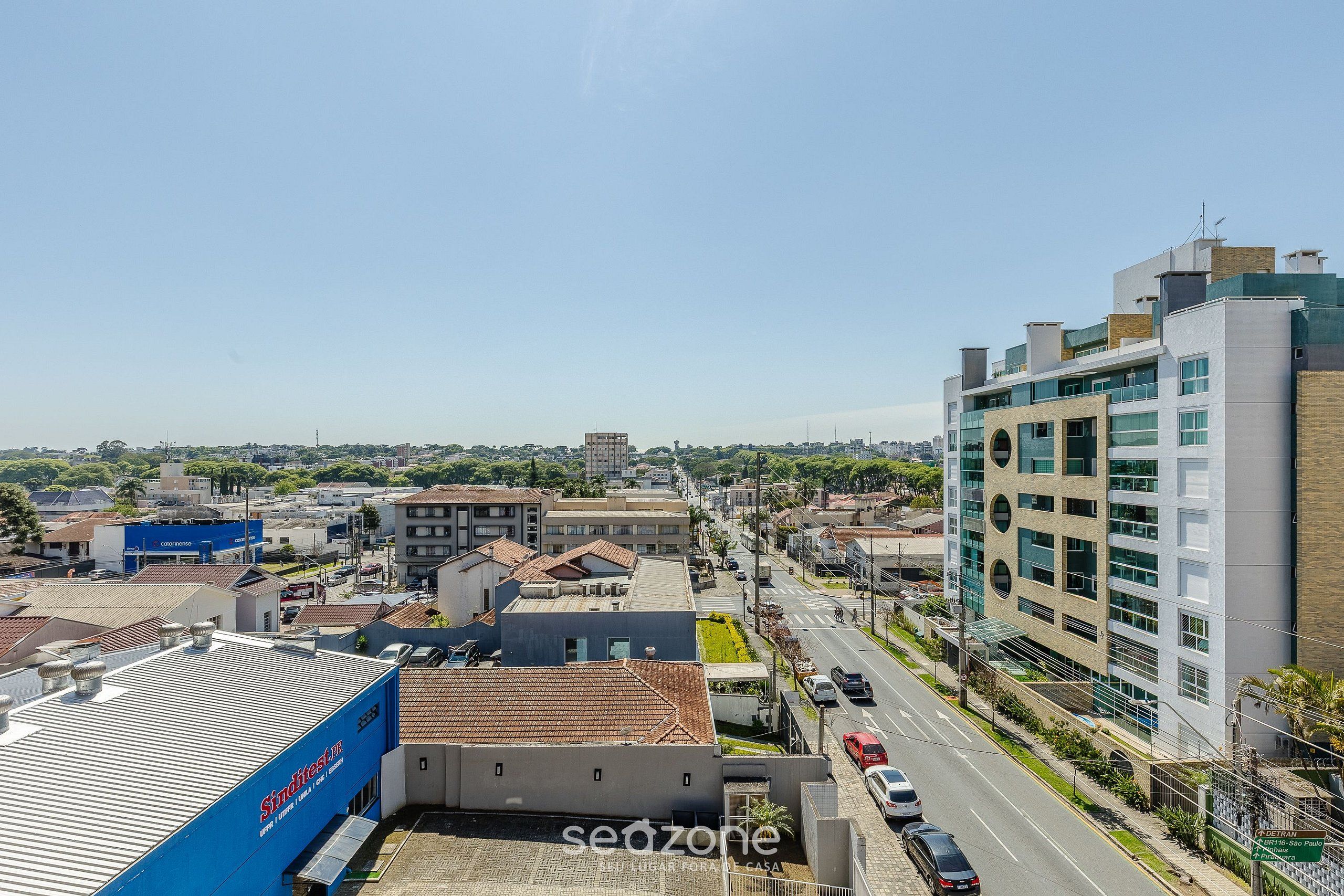 A cityscape with modern buildings, a clear sky, and a road with cars.