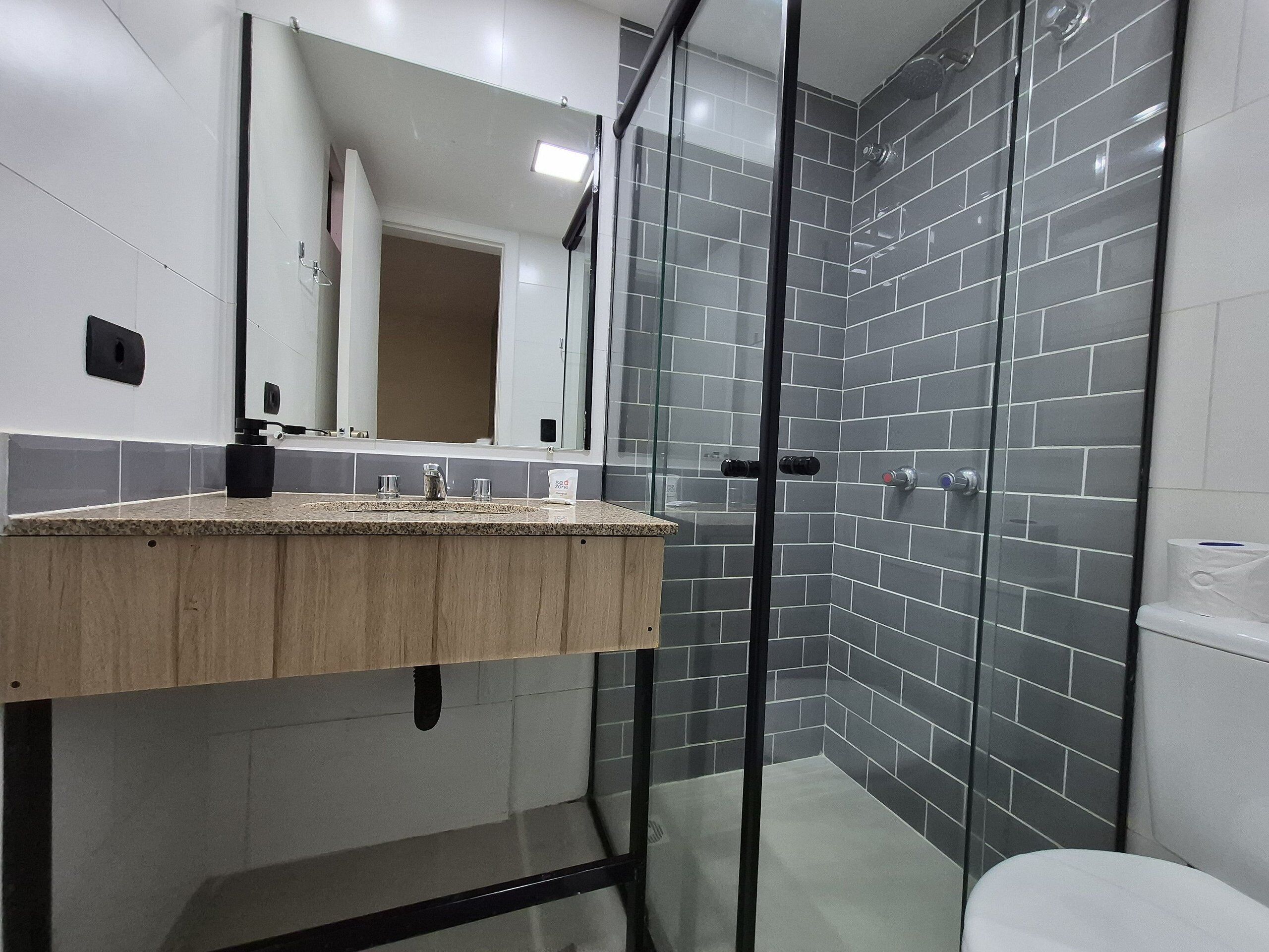 A modern bathroom with a wooden vanity, a glass shower enclosure, and grey tiled walls.