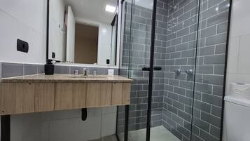 A modern bathroom with a wooden vanity, a glass shower enclosure, and grey tiled walls.