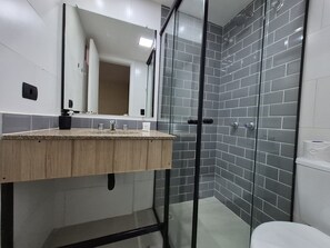 A modern bathroom with a wooden vanity, a glass shower enclosure, and grey tiled walls.