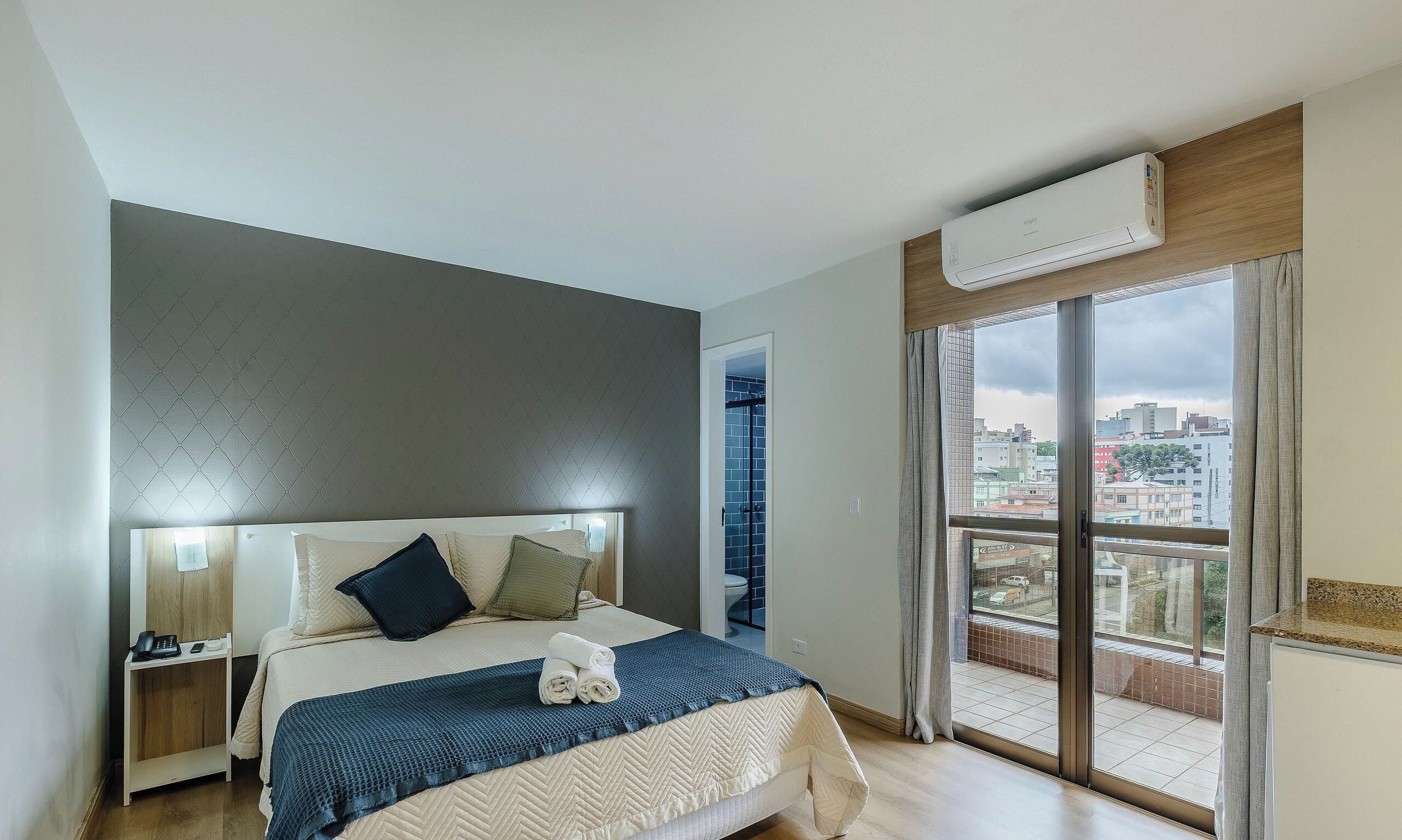 Une chambre d’hôtel comprenant un lit, des tables de chevet, une fenêtre donnant sur la ville et un appareil de climatisation.