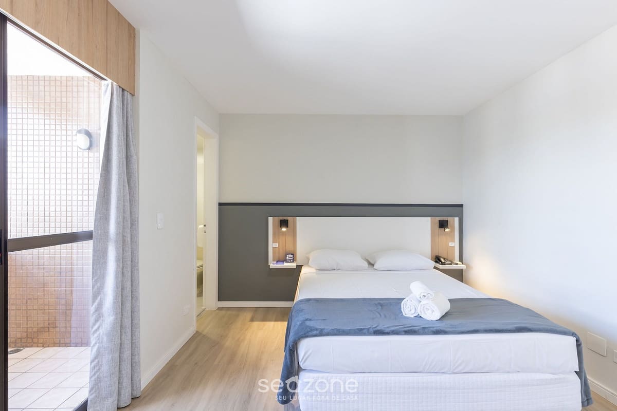 Una habitación de hotel moderna con una cama grande, una mesita de noche pequeña y una estantería empotrada.
