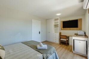 Un dormitorio con cama, escritorio, silla, armario y televisión empotrada.