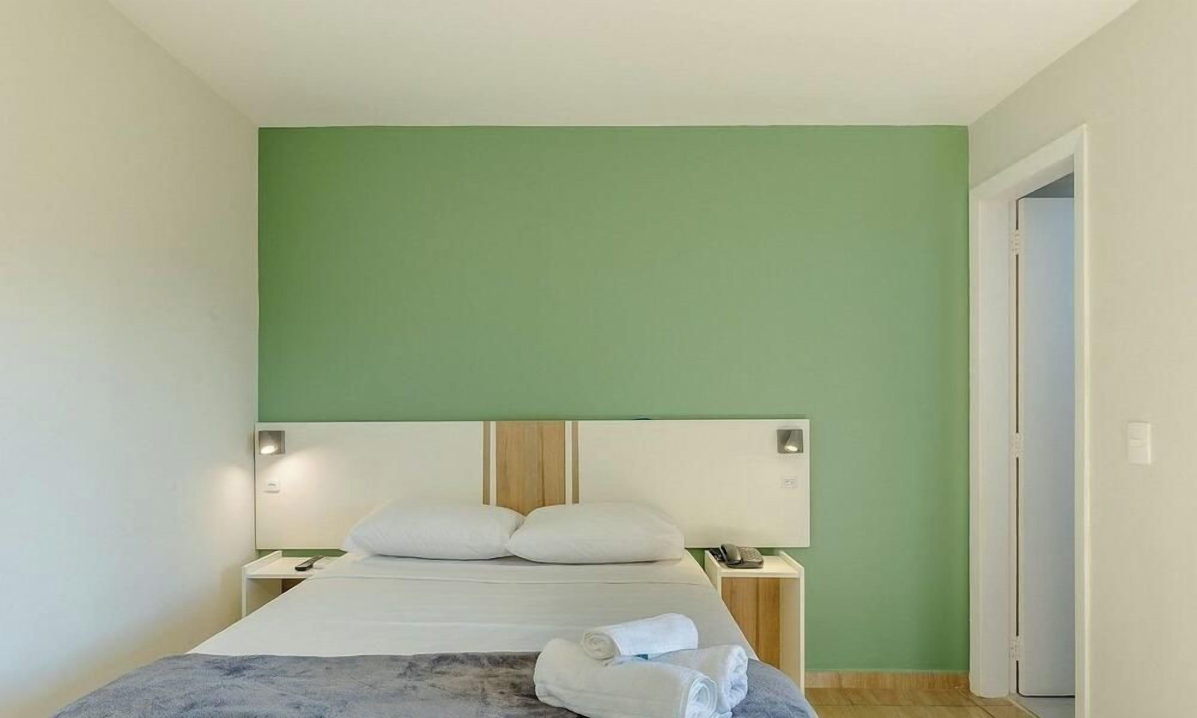 A single bed with a headboard, bedside tables, and a green wall.