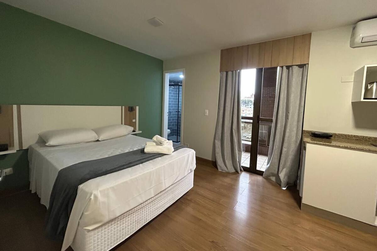 Een hotelkamer met een bed, een kleine kitchenette, een balkon met gordijnen en uitzicht.