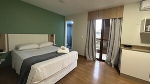 A hotel room with a bed, a small kitchenette, a balcony with curtains, and a view of the outside. - Studios at Upper Residence - Upps II (Curitiba)