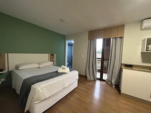 Une chambre d’hôtel avec un lit, une petite kitchenette, un balcon avec des rideaux et une vue sur l’extérieur.