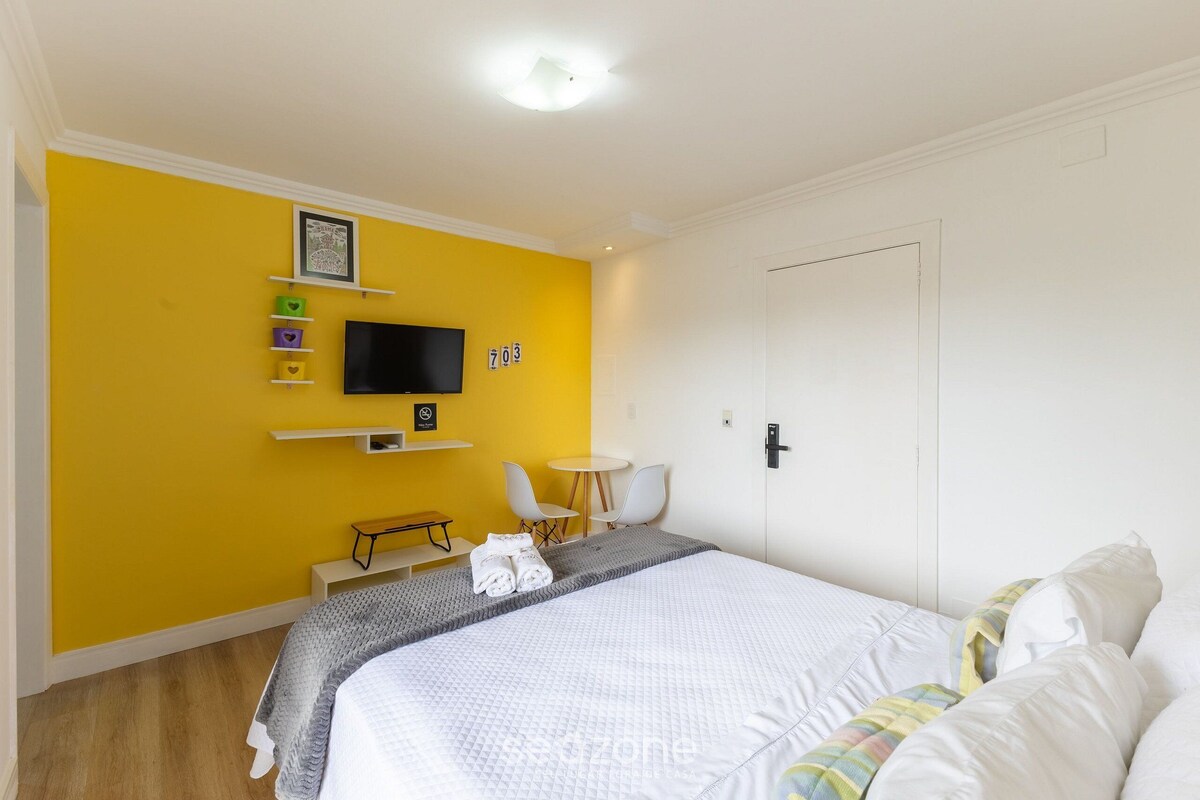A hotel room with a bed, a TV, a desk, a chair, and a small table.