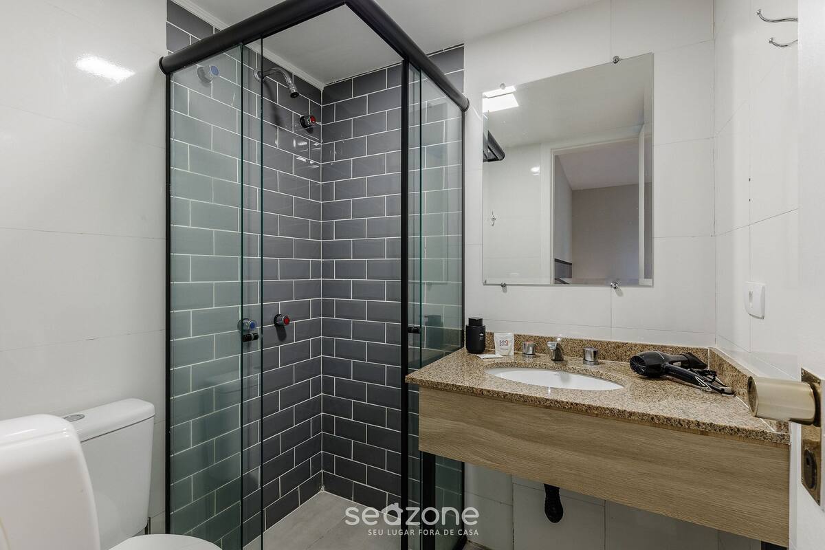 Een badkamer met een douchecabine van glas, een wastafel met een granieten blad en een spiegel boven de wastafel.
