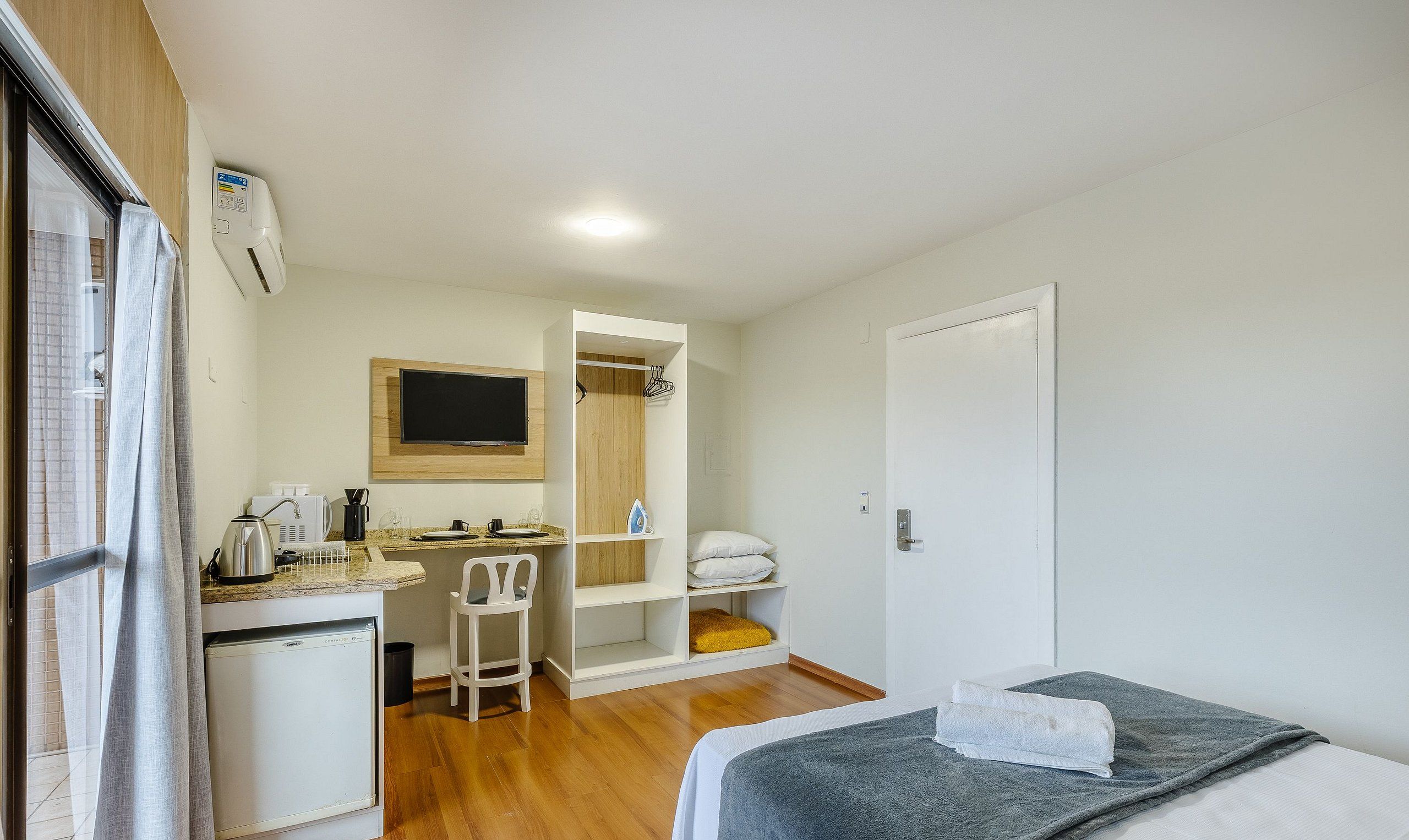 A compact room with a kitchenette, a bed, a small desk, and a TV.