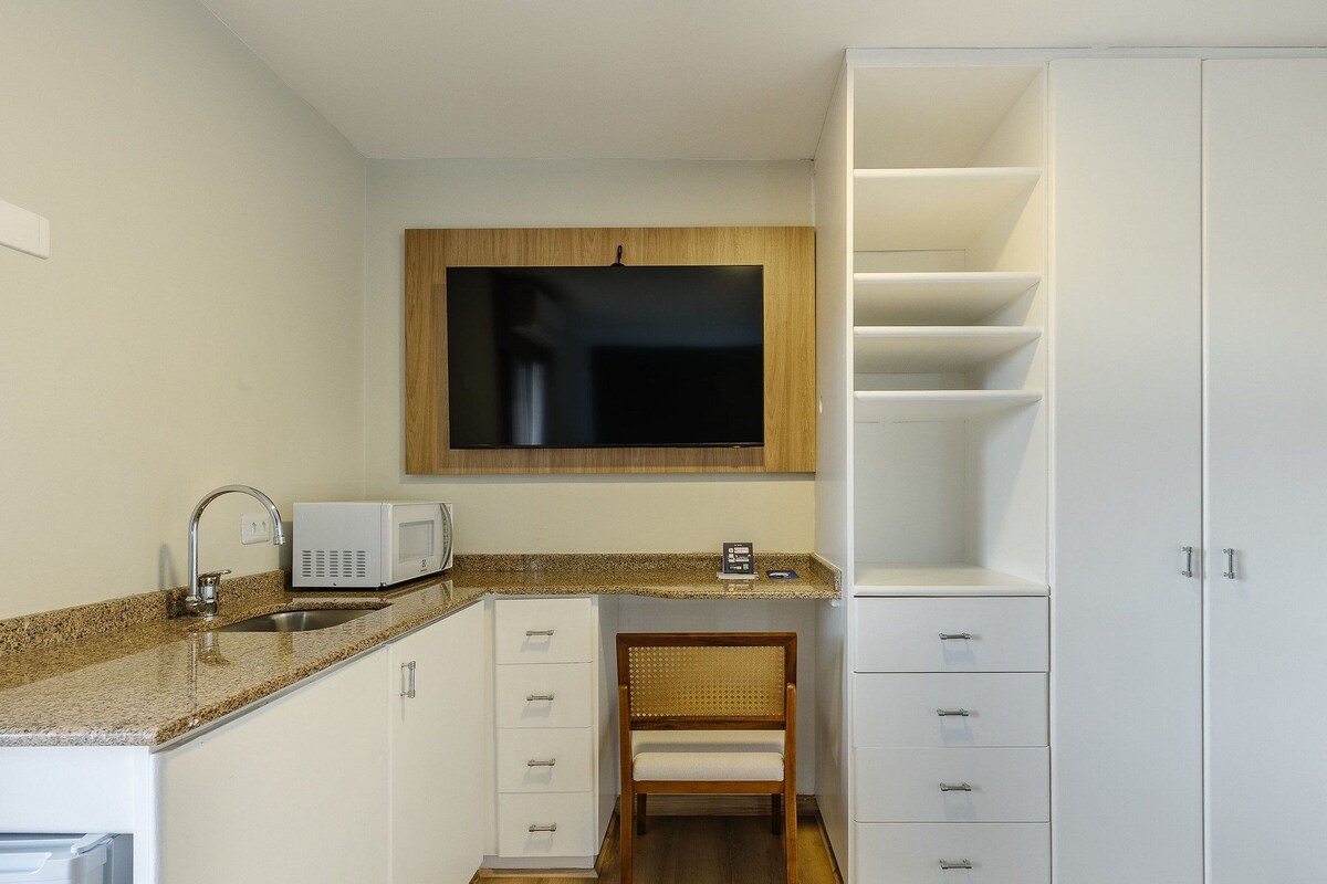 A compact kitchen with a microwave, sink, and a TV mounted above the counter.