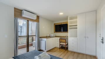 Quarto de hotel compacto com cama, cozinha compacta, banheiro e varanda.
