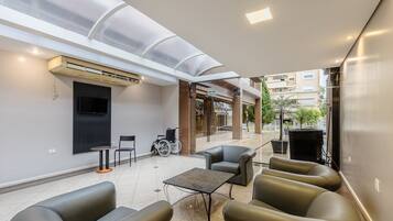 A modern outdoor seating area with a glass ceiling, a TV mounted on the wall, and a wheelchair.