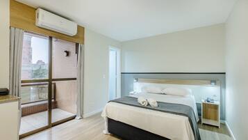Quarto de hotel com cama, mesa de cabeceira, janela com cortinas, ar condicionado e vista para edifícios.