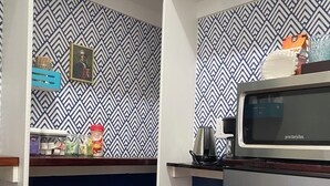 Eine Küche mit einer Mikrowelle, einer Kaffeemaschine und einem Kühlschrank. Der Rückwand ist gemustert und eine Wand ist blau akzentuiert.