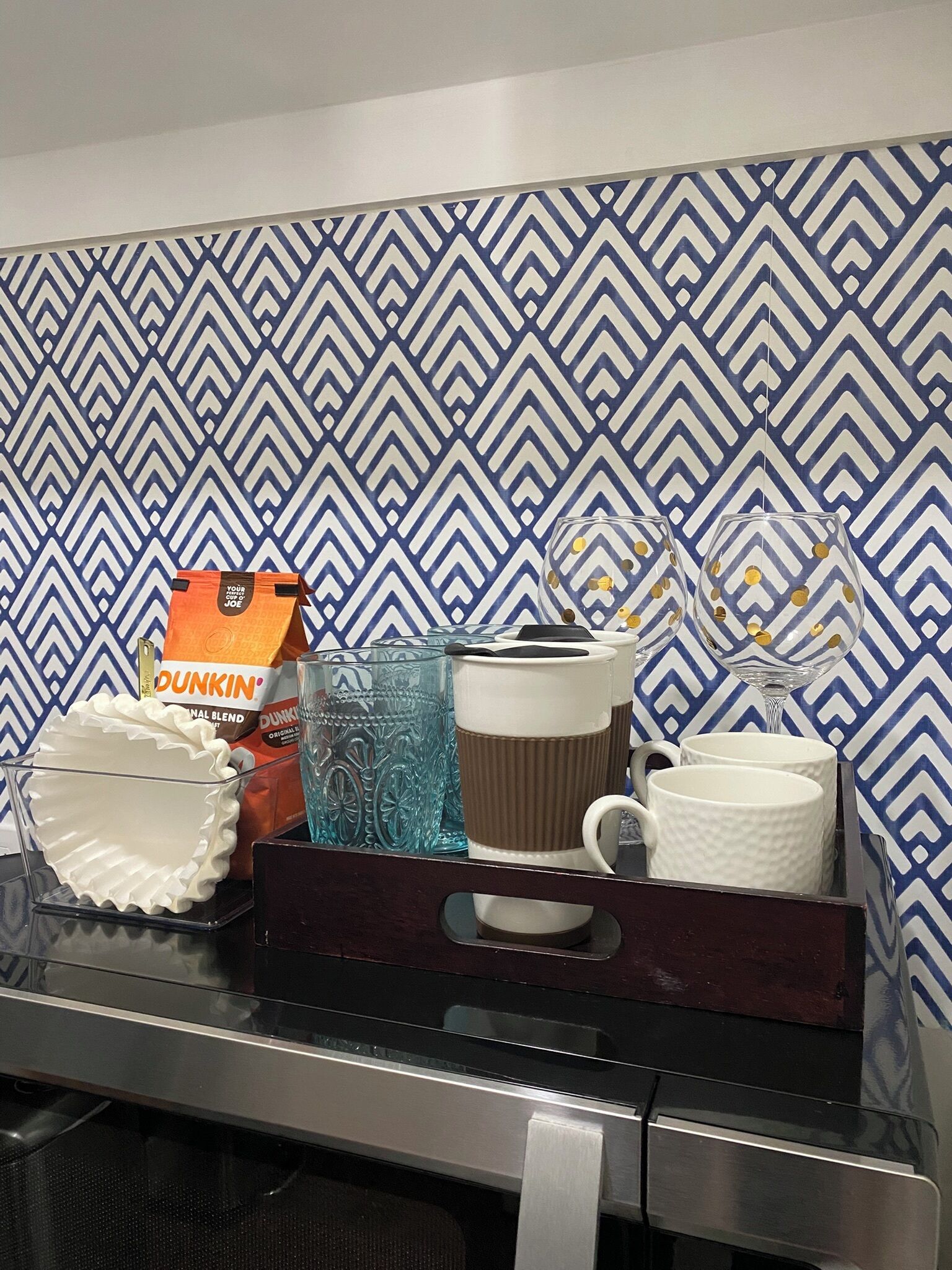 Uma bancada de cozinha com uma cafeteira, um saco de café Dunkin', um copo e uma caneca.