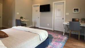 Ein Schlafzimmer mit einem Bett, einem Schreibtisch, einem Stuhl, einem Fernseher und einem kleinen Tisch mit einer Pflanze.
