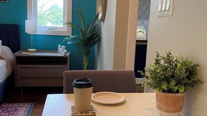 Ein gemütlicher Wohnraum mit Esstisch, einer Kaffeetasse, einem Teller, einer Topfpflanze und einem Bett mit blauer Kopfteil.