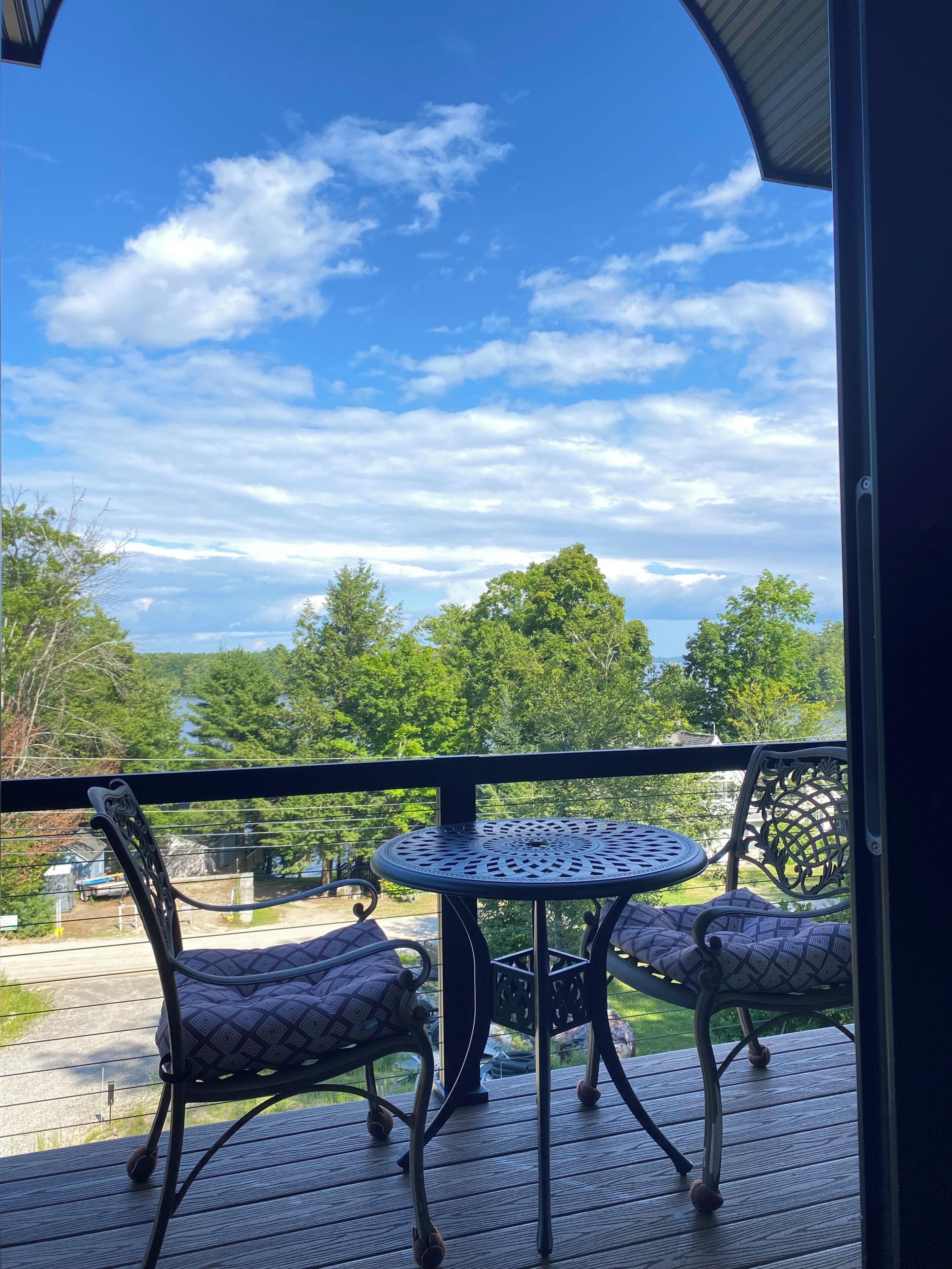 A balcony with a round table and two chairs, overlooking a scenic landscape with trees and a body of water.
