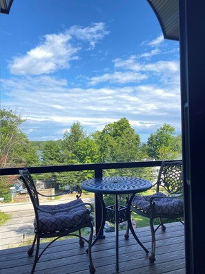 A balcony with a round table and two chairs, overlooking a scenic landscape with trees and a body of water. - Eagle Heights: luxurious Sebago Lake retreat sleeps 8+ (Sebago)