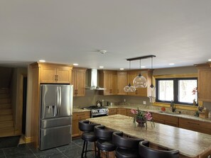 A modern kitchen with wooden cabinets, a stainless steel refrigerator, a gas stove, and a large island with bar stools. - Eagle Heights: luxurious Sebago Lake retreat sleeps 8+ (Sebago)
