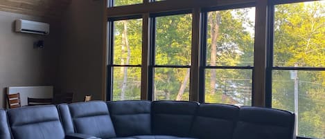 A modern living room with a large sectional sofa, a round coffee table, and a large window offering a view of trees.