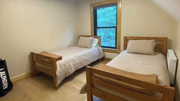 A small, well-lit room with two wooden beds, a window with a view of trees, and a ceiling light. - Eagle Heights: luxurious Sebago Lake retreat sleeps 8+ (Sebago)
