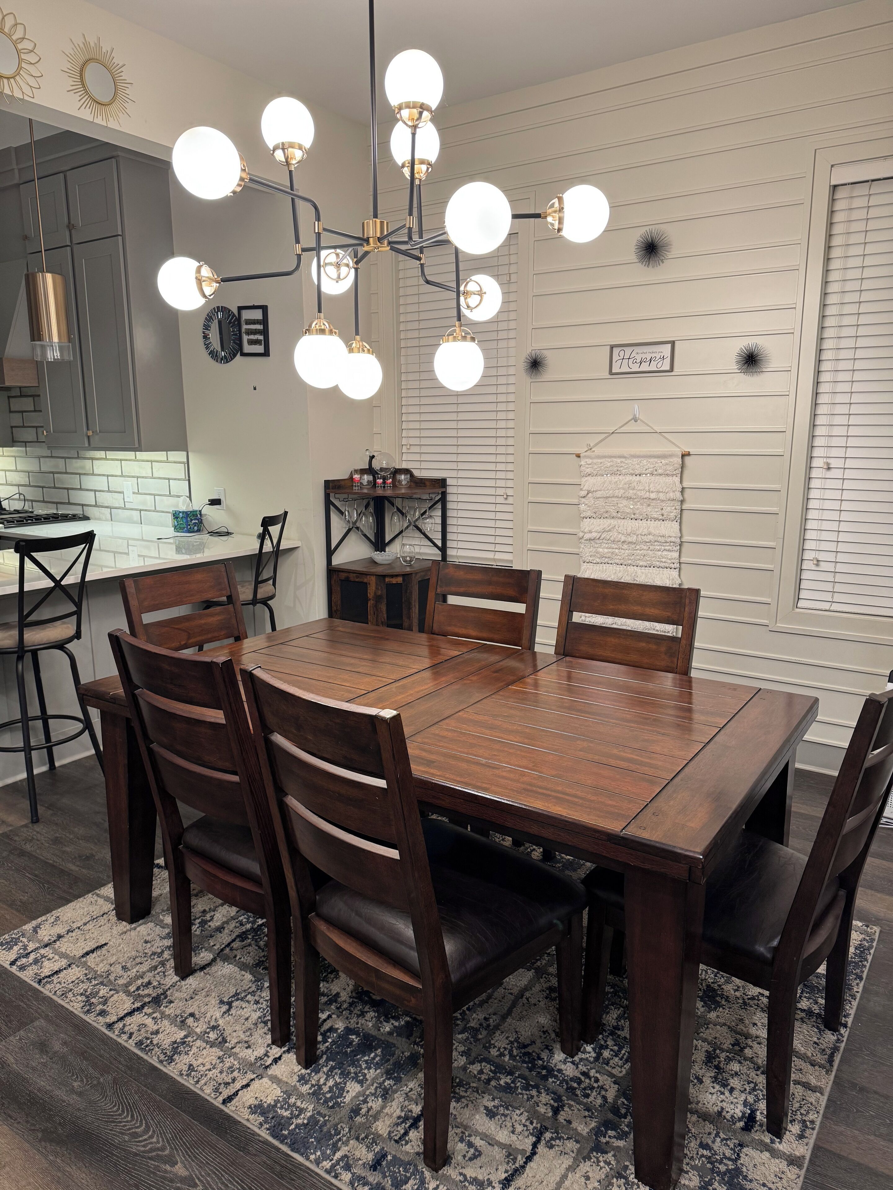 Un coin repas avec une table et des chaises en bois, un lustre et une cuisine en arrière-plan.