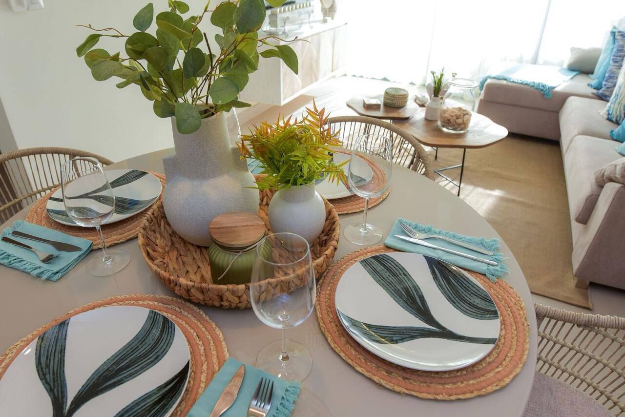 A dining area with a round table set for four, featuring woven placemats, leaf-patterned plates, and clear glassware.