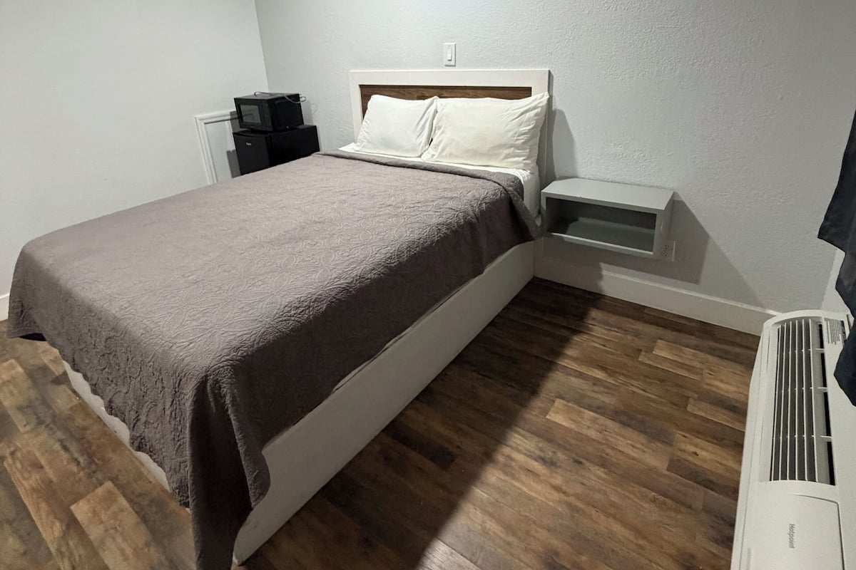 Une chambre à coucher comprenant un lit, une table de chevet, un radiateur et une prise électrique fixée au mur.