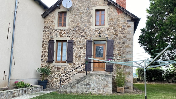 A stone house with a wooden door, two windows with shutters, a satellite dish, and a small garden. - Gite du bousquet (Cassagnes-Bégonhès)